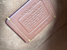 Load image into Gallery viewer, Close-up of a Coach interior leather patch with embossed branding and text on a taupe fabric background.