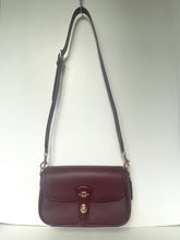 Load image into Gallery viewer, A burgundy pebbled leather crossbody handbag with a black shoulder strap and silver-tone hardware, shown against a plain white background.