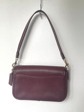 Load image into Gallery viewer, A dark plum purple pebbled leather shoulder bag with a single strap and silver-tone hardware, hanging against a plain white wall.