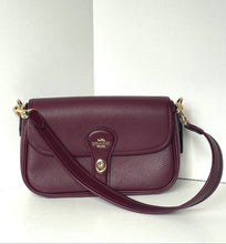 Load image into Gallery viewer, A Coach pebbled leather shoulder bag in deep burgundy, featuring a gold-tone logo medallion on the front flap and a matching burgundy strap with gold hardware, set against a plain white background.