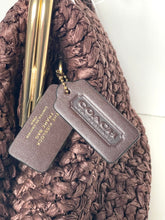 Load image into Gallery viewer, A close-up of a brown woven bag with two Coach leather hang tags attached, one embossed with the Coach logo and the other showing 'PREMIER LOCK' and 'PETER BURGESS COLLECTION'.