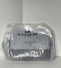 Load image into Gallery viewer, A Coach New York handbag wrapped in clear plastic packaging, showing the black Coach logo and horse-and-carriage emblem on the front label.