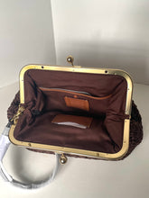 Load image into Gallery viewer, An open woven brown handbag with a gold-tone metal frame, showing a brown fabric interior with a slip pocket and a small leather patch.