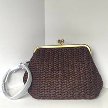 Load image into Gallery viewer, A dark brown knitted clutch purse with a gold-tone kiss-lock frame and a white protective paper sleeve wrapped around its handle, set against a plain light gray background.