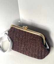 Load image into Gallery viewer, A dark brown woven straw clutch bag with a gold-tone metal kiss-lock frame and pearl accents, resting on a white surface against a white background.