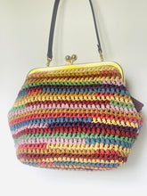 Load image into Gallery viewer, A handmade crocheted handbag with horizontal stripes of multiple colors including pink, blue, green, yellow, and orange, featuring a black shoulder strap and a gold-tone metal frame clasp.