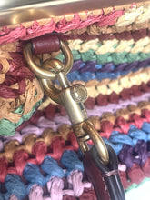 Load image into Gallery viewer, Close-up of a woven multicolor bag with a brass-tone metal swivel clasp and dark brown leather strap attachment.