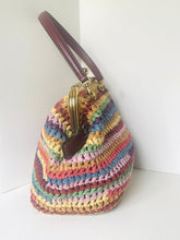 Load image into Gallery viewer, A handmade crochet handbag with horizontal stripes of multiple pastel and earthy colors, featuring a dark brown leather handle and a gold-tone metal clasp closure.