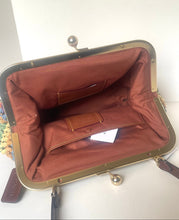 Load image into Gallery viewer, An open vintage-style kiss-lock handbag with a warm brown fabric lining and a brass-tone metal frame, shown against a plain white background.
