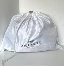 Load image into Gallery viewer, A white Coach branded satin dust bag with silver drawstrings and a silver horse-and-carriage logo, resting on a light gray surface against a neutral light gray background.