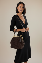 Load image into Gallery viewer, A woman wearing a bohemian floral print maxi dress and carrying a dark brown woven handbag with a gold-tone kiss-lock frame, standing in a modern living room setting.