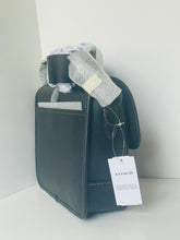 Load image into Gallery viewer, A Coach black leather shoulder bag with a white brand hangtag, wrapped in protective bubble wrap and a gray ribbon at the top, set against a plain white background.