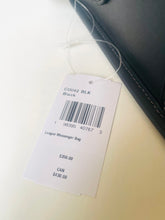 Load image into Gallery viewer, A white product tag for a League Messenger Bag, showing the color as 'BLK' and price $350.00, attached to a black leather bag on a light cream background.