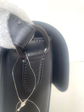Load image into Gallery viewer, Close-up of a black leather handbag showing a strap attachment with a dark metal ring, contrast stitching, and a hangtag.