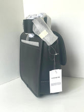 Load image into Gallery viewer, A Coach black leather handbag with a black shoulder strap, wrapped in protective silver foil and a white COACH hangtag, set against a plain white background.