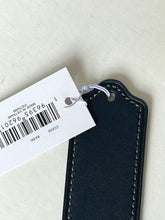 Load image into Gallery viewer, A close-up of a black leather keychain or tag with white stitching, attached to a white barcode price tag, on a light beige textured background.