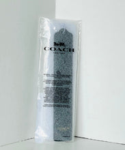 Load image into Gallery viewer, A Coach pre-rolled travel towel in its clear plastic packaging, standing upright against a white corner wall.