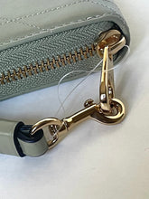 Load image into Gallery viewer, Close-up of a light gray quilted leather zip-around wallet with a gold-tone metal clasp and a clear protective plastic film still attached.