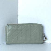 Load image into Gallery viewer, A light sage green quilted zip-around wallet with a diagonal stitched pattern and a small gold-tone zipper pull, shown against a minimalist white and gray background.