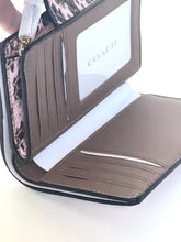 Load image into Gallery viewer, An open Coach wallet in taupe-brown leather with a pink and black snakeskin-patterned interior panel, showing card slots, a white ID window with the Coach logo, and a white strap.