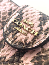 Load image into Gallery viewer, Close-up of a Coach New York wallet or pouch featuring a pink and black python pattern, with gold-tone metal logo hardware.