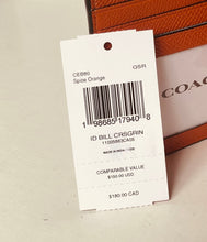 Load image into Gallery viewer, A white COACH Spice Orange garment tag with a barcode and product details, shown in front of an orange leather Coach bag on a light beige surface.