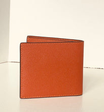 Load image into Gallery viewer, A textured orange leather bifold wallet standing upright on a light surface against a white background.