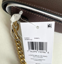 Load image into Gallery viewer, Close-up of a brown leather handbag with a gold chain strap and a white product tag showing barcode and item details.