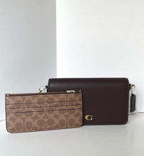 Load image into Gallery viewer, A Coach crossbody bag in dark brown pebbled leather with a gold C logo, shown next to a matching brown signature canvas zip pouch on a light gray background.
