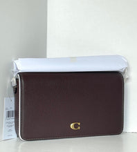 Load image into Gallery viewer, A dark brown pebbled leather crossbody bag with a gold 'C' logo on the front, resting on a white surface with its white dust bag and product tag visible.