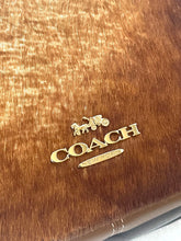 Load image into Gallery viewer, Close-up of a Coach logo on a brown leather surface