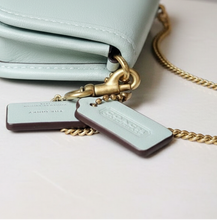 Load image into Gallery viewer, Light blue Coach wallet with gold chain and tags on a textured surface