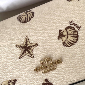 Close-up of a Coach handbag with shell and starfish patterns on a beige background.