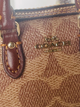 Load image into Gallery viewer, Close-up of a Coach handbag with brown leather strap and logo.