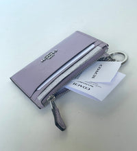 Load image into Gallery viewer, A Coach zip-around card holder wallet in light lavender leather, shown with its silver-tone hardware, keyring, and branded white tags on a light gray surface.