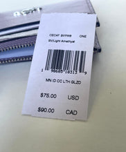 Load image into Gallery viewer, A close-up of a white paper product tag with a barcode and pricing information, placed over a light purple zippered wallet on a light surface.