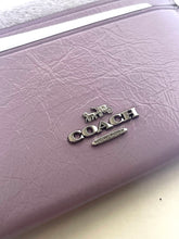 Load image into Gallery viewer, A close-up of a Coach wallet in textured lavender purple leather, featuring the silver-tone metallic Coach logo and horse-and-carriage emblem on the front.