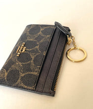 Load image into Gallery viewer, Black patterned wallet with gold zipper and keychain on a beige background
