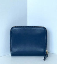 Load image into Gallery viewer, A dark navy blue leather zip-around wallet with gold-tone hardware, standing upright in a corner against a light blue background.