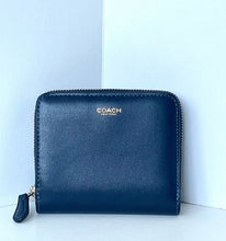 Load image into Gallery viewer, A Coach zip-around wallet in dark navy blue leather with gold-tone hardware and the gold 'COACH' logo on the front, set against a light blue and white background.