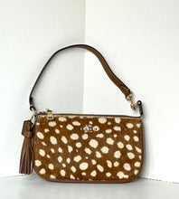 Load image into Gallery viewer, A Coach crossbody handbag featuring a brown and cream spotted animal print, a brown leather strap, and a matching leather tassel, displayed against a white background.