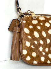 Load image into Gallery viewer, A close-up of a brown and cream spotted hair-on-hide handbag with tan leather trim, a tassel charm, and gold-tone hardware against a white background.