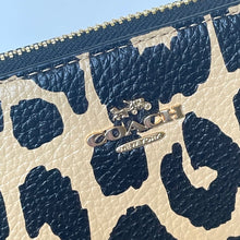 Load image into Gallery viewer, Close-up of a Coach wallet with navy leaf pattern on beige background