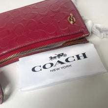 Load image into Gallery viewer, Red Coach wallet on a white surface with a Coach New York pouch underneath.