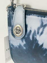 Load image into Gallery viewer, Close-up of a Coach handbag in blue and white tie-dye leather with a silver-tone metal snap button and zipper.
