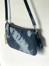 Load image into Gallery viewer, A small shoulder bag with a glossy navy and white tie-dye pattern, featuring a silver zipper, silver hardware, and a matching leather charm with a keychain ring, shown against a plain white wall.