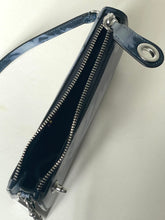 Load image into Gallery viewer, A glossy dark blue patent leather wristlet clutch with silver-tone hardware, shown open to reveal its interior. The clutch features a matching blue strap with a silver-tone metal grommet and a small chain detail.