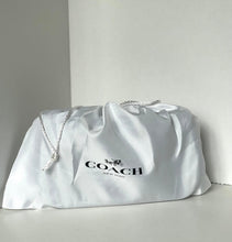 Load image into Gallery viewer, A white Coach dust bag with the black COACH logo and horse-and-carriage mark, resting on a light gray surface against a light gray background.