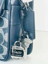 Load image into Gallery viewer, Close-up of a Coach leather product with keychain and strap on a white background