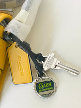 Load image into Gallery viewer, Coach keychain with bottle cap charm and key on a white background